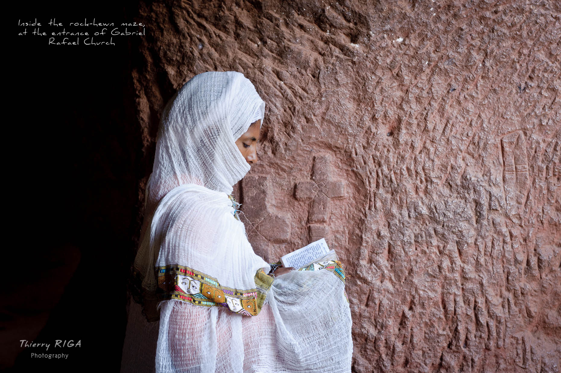 Lonely woman in white dress prying in Gabriel Raphael church in Lalibela, Ethiopia, Thierry Riga