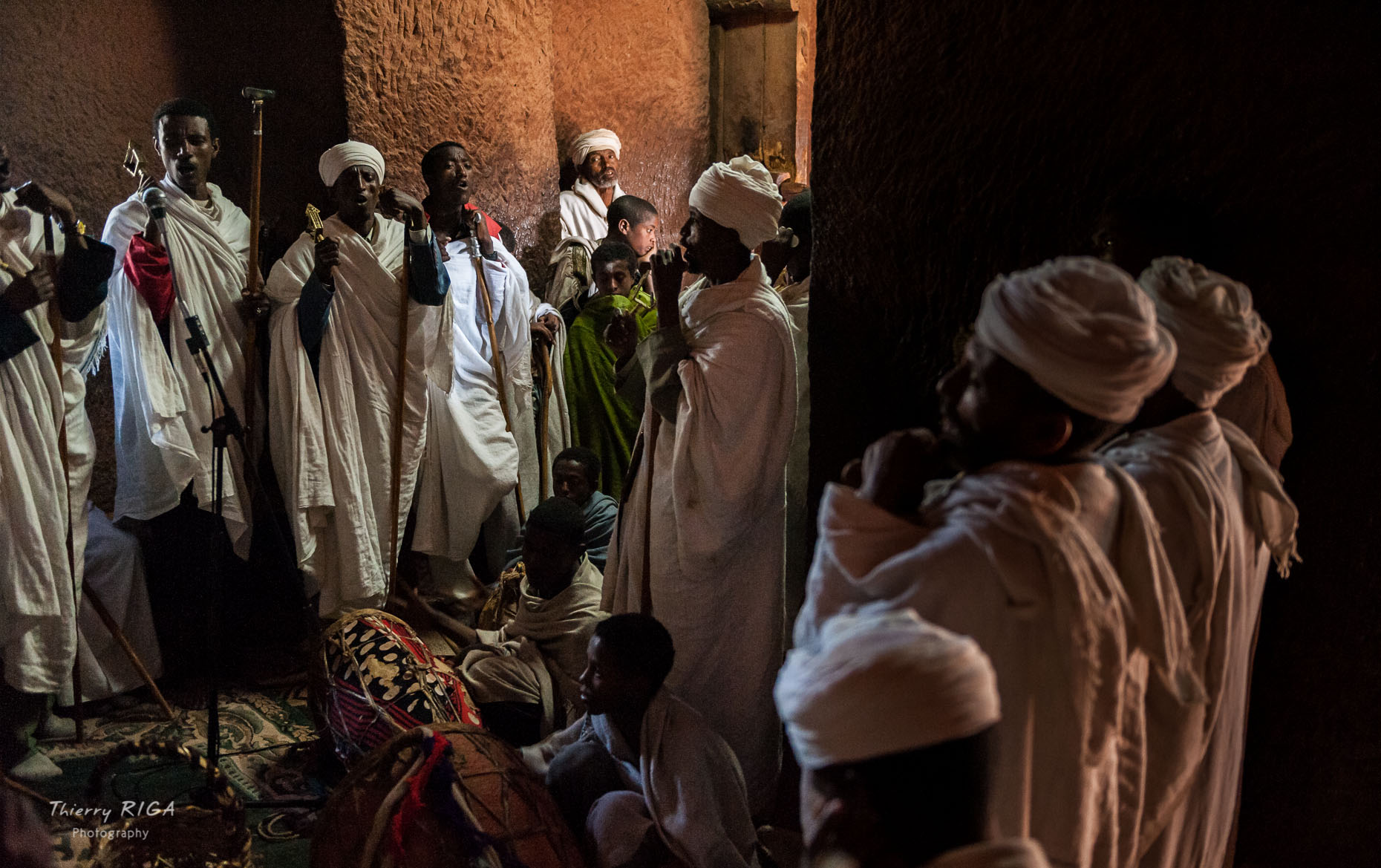 Group of priests with white dresses chanting in the dark corner of Gabriel Raphael church in Lalibela, Ethiopia